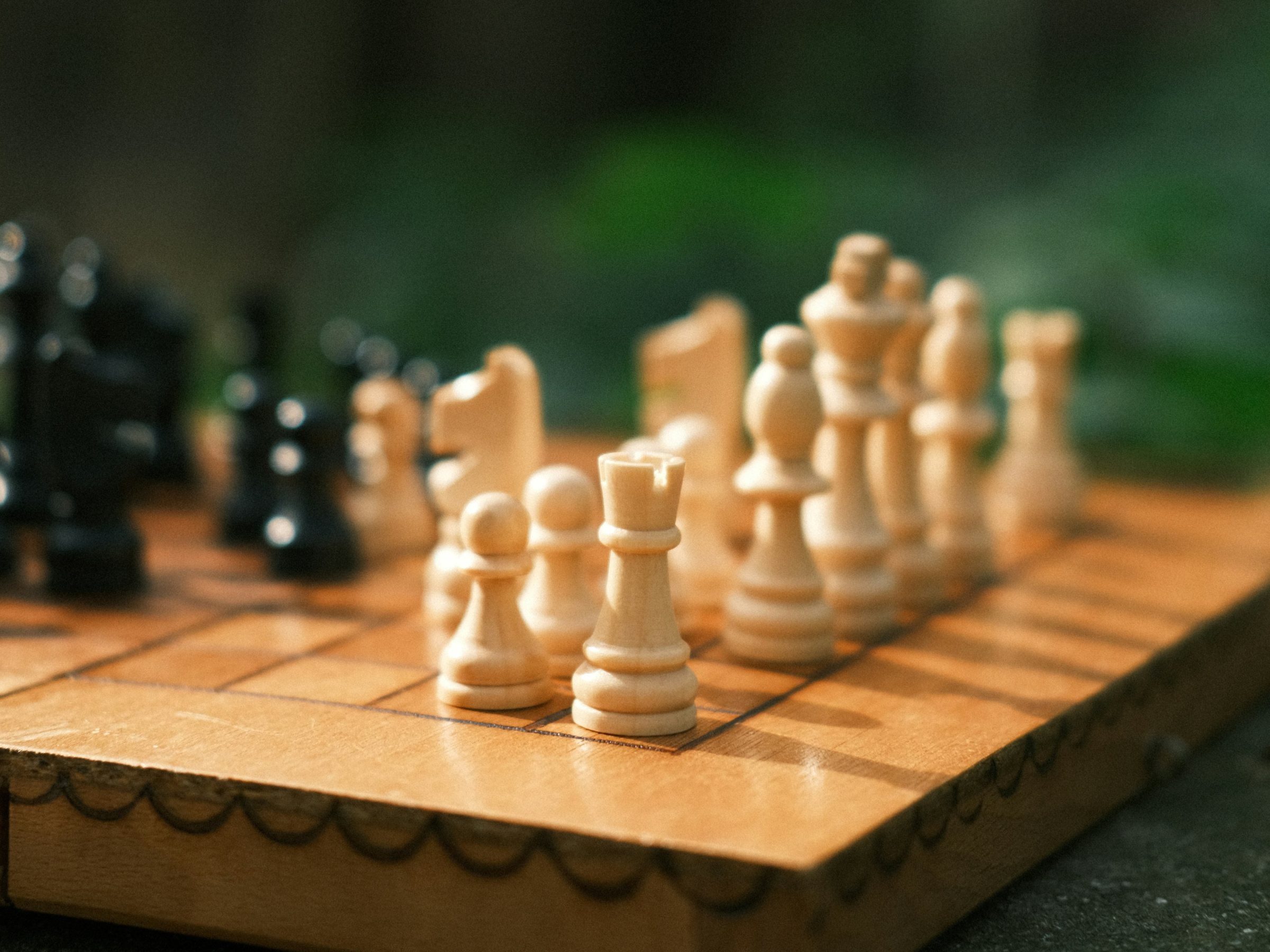 A wooden chess board mid-game, the white pieces in the light